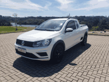 a white volkswagen truck is parked on a brick driveway with a lake in the background