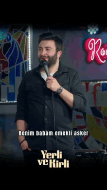 a man holding a microphone in front of a sign that says ' benim babam emekli asker ' on it