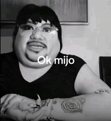 a black and white photo of a man with glasses and a tattoo on his arm that says ok mijo