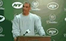 a man is standing at a podium with a microphone in front of a green wall with ny logos on it .