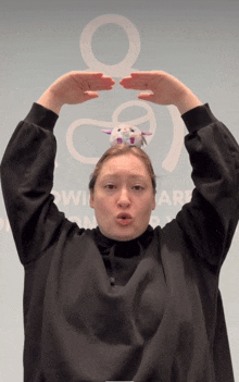 a woman wearing a black sweatshirt has a stuffed animal on her head in front of a sign that says wincare