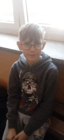 a young boy wearing glasses is sitting on a window sill .