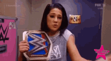 a woman is holding a wrestling championship belt in front of a sign that says bayley .