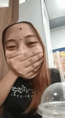 a woman is covering her mouth with her hand while sitting in front of a cup of coffee .