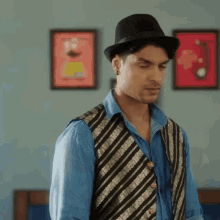 a man wearing a hat and a vest is standing in front of a wall with pictures on it