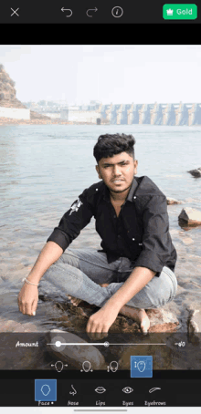 a man in a black shirt is sitting on a rock near the water