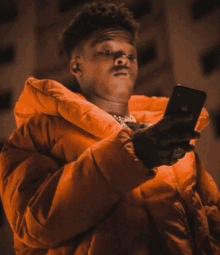 a young man in an orange jacket is holding a cell phone