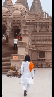 a man in a white shirt walks in front of a large temple