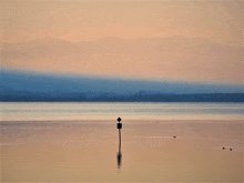 a sign on a pole in the middle of a lake with mountains in the background