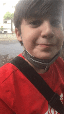 a young boy wearing a red shirt and a black shoulder strap