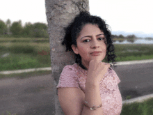 a woman with curly hair leans against a tree