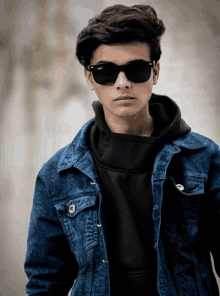 a boy wearing sunglasses and a denim jacket looks at the camera