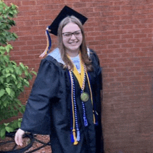 a young woman in a graduation cap and gown is smiling while standing in front of a brick wall .