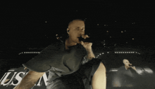 a man singing into a microphone in front of a sign that says ' us '