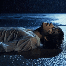 a woman in a white shirt is laying in the rain