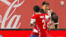 a group of soccer players hugging each other in front of a coca cola ad