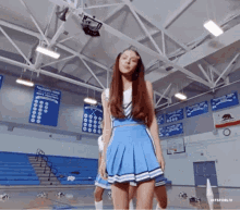 a cheerleader in a blue skirt is standing in a gym with a banner that says palisades high on it