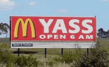 a mcdonald 's billboard that says `` m yass open 6 am '' is sitting in the middle of a field .