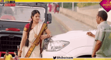 a woman in a sari is standing next to a man in a green shirt in front of a ford car