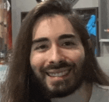 a close up of a man with long hair and a beard smiling .