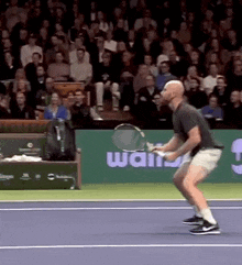 a man is holding a tennis racquet on a tennis court in front of a wall that says " wait "