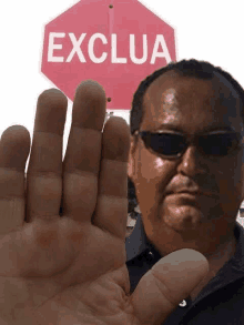 a man wearing sunglasses is holding his hand up in front of a sign that says exclua