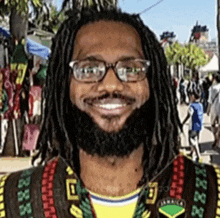 a man with dreadlocks and glasses is smiling in front of a crowd of people