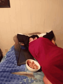 a person wrapped in a blanket is sleeping on a bed next to a bowl of crackers .