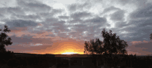 a sunset with a house in the foreground and trees in the foreground