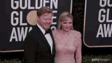 a man and a woman are posing for a picture in front of a sign that says golden globe awards