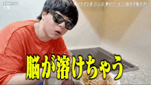 a man wearing sunglasses and a red shirt is eating ramen in a kitchen