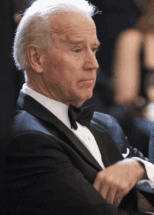 a man in a tuxedo sits with his hand on his shoulder