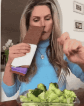 a woman is eating broccoli with a fork while holding a chocolate bar