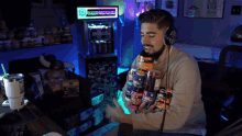 a man wearing headphones holds a stack of protein powders in front of a vending machine that says fully loaded