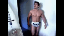 a shirtless wrestler in white underwear is standing in a room .