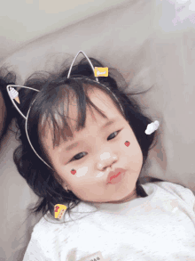 a little girl wearing a cat ear headband has stickers on her face including one that says ' love '