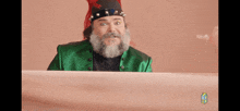 a man with a beard and a green jacket is sitting at a desk