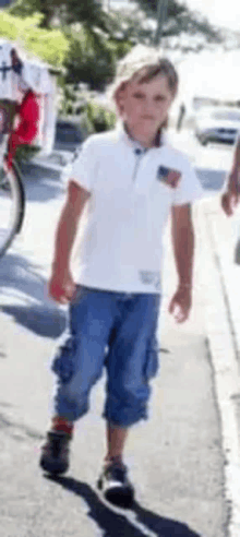 a young boy in a white shirt and blue pants is walking down the street