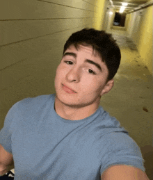 a young man in a blue shirt taking a selfie in a hallway