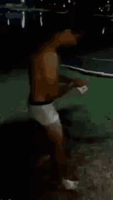 a shirtless man in white underwear is standing on a basketball court at night .