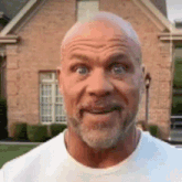 a bald man with a beard is smiling in front of a brick building .