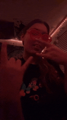 a woman wearing red sunglasses is smoking a cigarette in a dark room