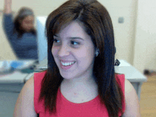 a woman in a red tank top is smiling with a blurry background