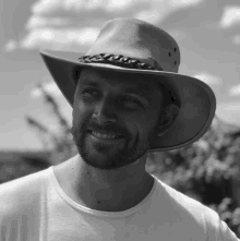 a man wearing a cowboy hat and a white shirt smiles in a black and white photo