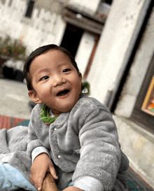 a baby wearing a grey jacket is smiling and looking at the camera