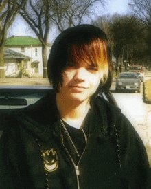 a young boy with red and blonde hair is standing in front of a car on a street .