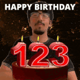 a man stands in front of a birthday cake with candles in the shape of 123