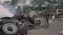 a man standing in front of a pile of junk including a barrel that says ' lg ' on it