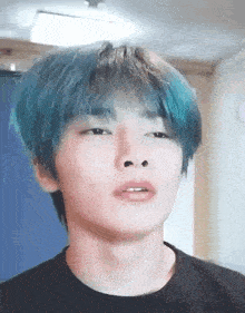 a young man with blue hair is making a funny face while wearing a black shirt .