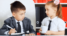 a boy and a girl are sitting at a desk with binders in the background